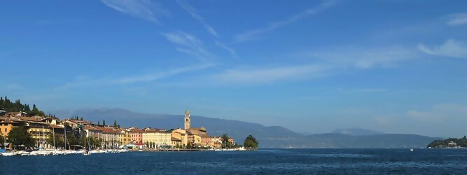 Trip Angebote beliebte Urlaubsziele am Gardasee -  Mit einer Fläche von 370 km² ist der Gardasee der größte See Italiens. Es liegt am Fuße der Alpen und erstreckt sich über drei Staaten: Lombardei, Venetien und Trentino. Die maximale Tiefe des Sees beträgt 346 m, er hat eine längliche Form und sein nördliches Ende ist sehr schmal. Dort ist der See von den Bergen der Gruppo di Baldo umgeben. Du trittst aus deinem gemütlichen Hotelzimmer und es begrüßt dich die warme italienische Sonne. Du blickst auf den atemberaubenden Gardasee, der in zahlreichen Blautönen schimmert - von tiefem Dunkelblau bis zu funkelndem Türkis. Majestätische Berge umgeben dich, während die Brise sanft deine Haut streichelt und der Duft von blühenden Zitronenbäumen deine Nase kitzelt. Du schlenderst die malerischen, engen Gassen entlang, vorbei an farbenfrohen, blumengeschmückten Häusern. Vereinzelt unterbricht das fröhliche Lachen der Einheimischen die friedvolle Stille. Du fühlst dich wie in einem Traum, der nicht enden will. Jeder Schritt führt dich zu neuen Entdeckungen und Abenteuern. Du probierst die köstliche italienische Küche mit ihren frischen Zutaten und verführerischen Aromen. Die Sonne geht langsam unter und taucht den Himmel in ein leuchtendes Orange-rot - ein spektakulärer Anblick.